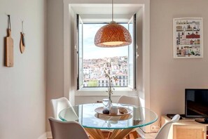 A dining area with a glass table, white chairs, a hanging woven light fixture, and a cityscape view through a window. - Casa das Fontainhas - Center Lisbon (Lisbon)