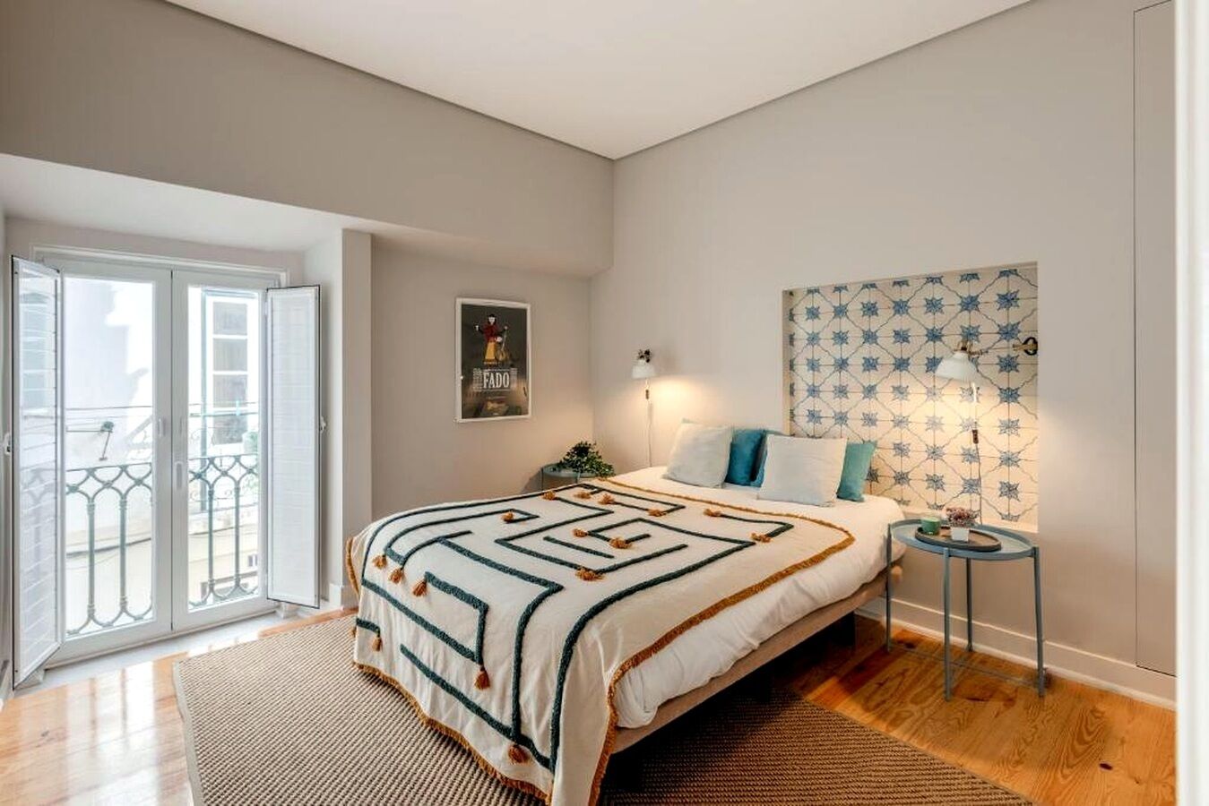 Una camera da letto con un letto, un comodino, una lampada, un poster appeso al muro e una porta finestra.