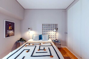 Een slaapkamer met een bed, nachtkastjes, een wandlamp, een poster en een behang met patroon.