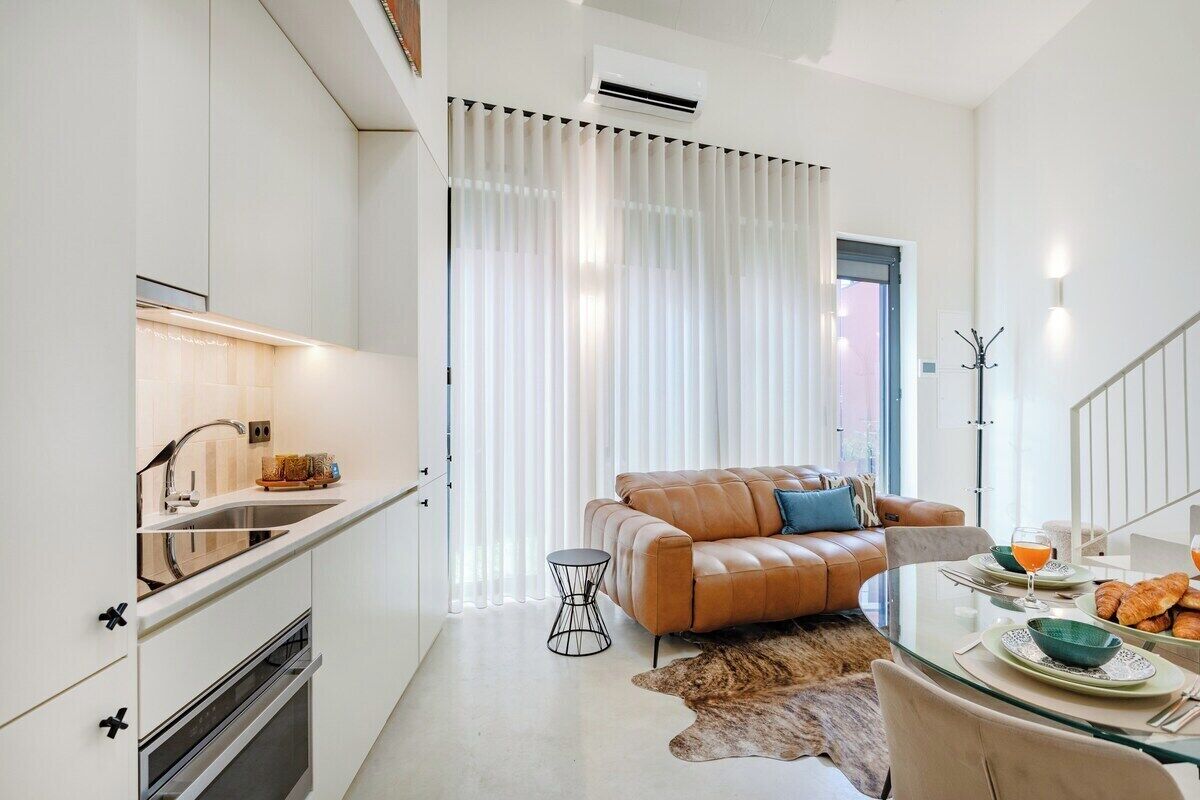 A modern kitchen with a built-in oven, a dining area with a glass table, and a leather sofa.