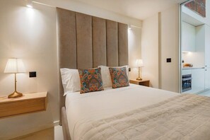 A hotel room with a large bed, two bedside tables with lamps, a headboard, and a view of a kitchen area. - Porto Center Duplex | Edifício Terracotta (Porto)