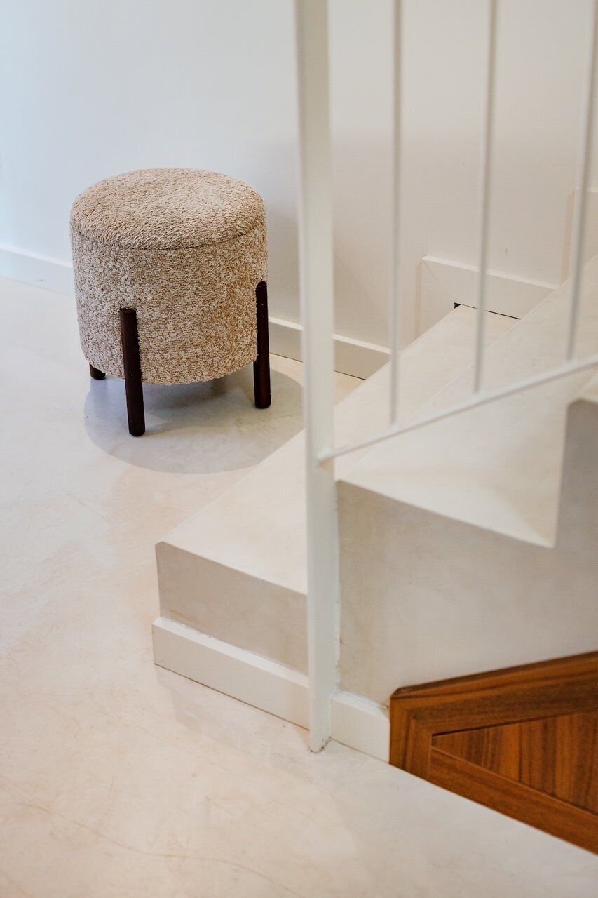 Een trap met een witte leuning en een beige poef met houten poten.