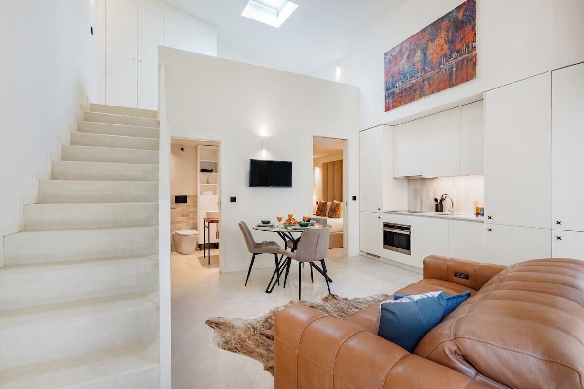 A modern interior with a staircase, a dining area, a kitchen, and a living room with a leather sofa.