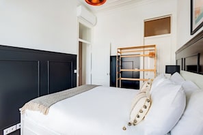 A bedroom with a bed, a wooden ladder, a white wall, and a door. - Graça's Urban Elegance (Lisbon)