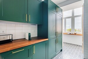 A kitchen with teal cabinets, a wooden countertop, and a window with a view. - Graça's Urban Elegance (Lisbon)