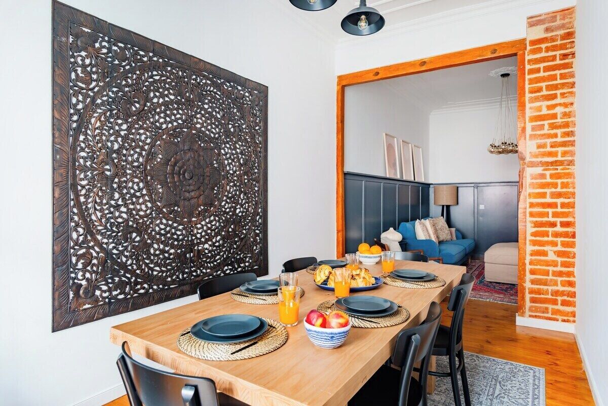 Un coin repas avec une table en bois, des assiettes noires et un panneau décoratif au mur.
