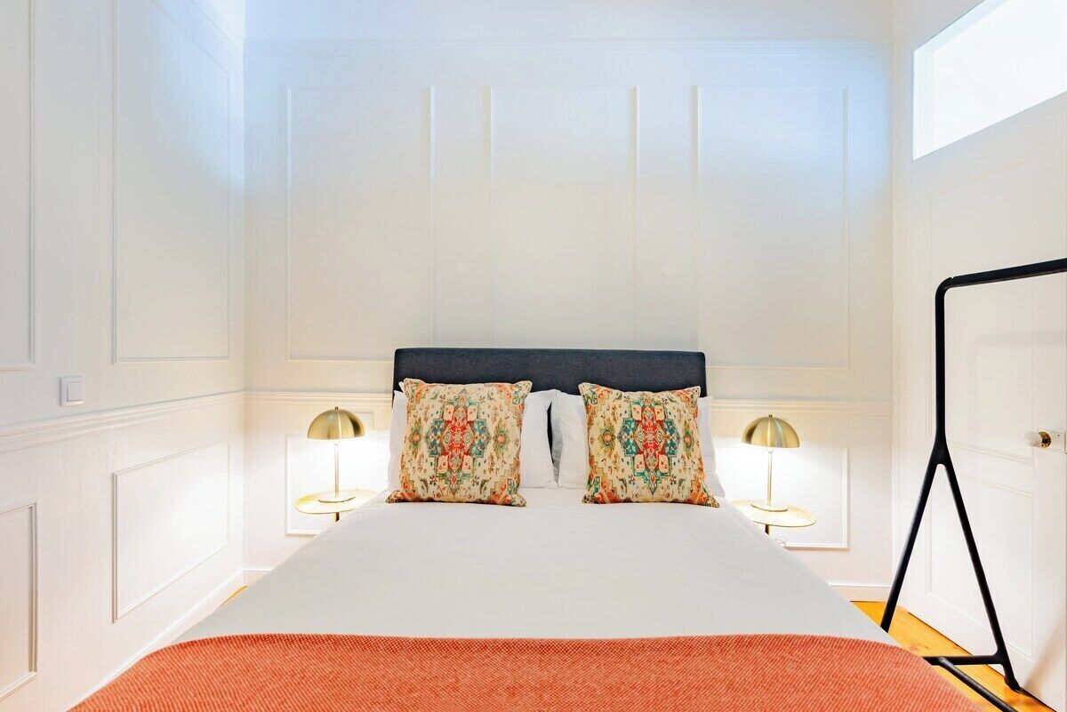 A hotel room with a large bed, two decorative pillows, two bedside lamps, and a black floor lamp.