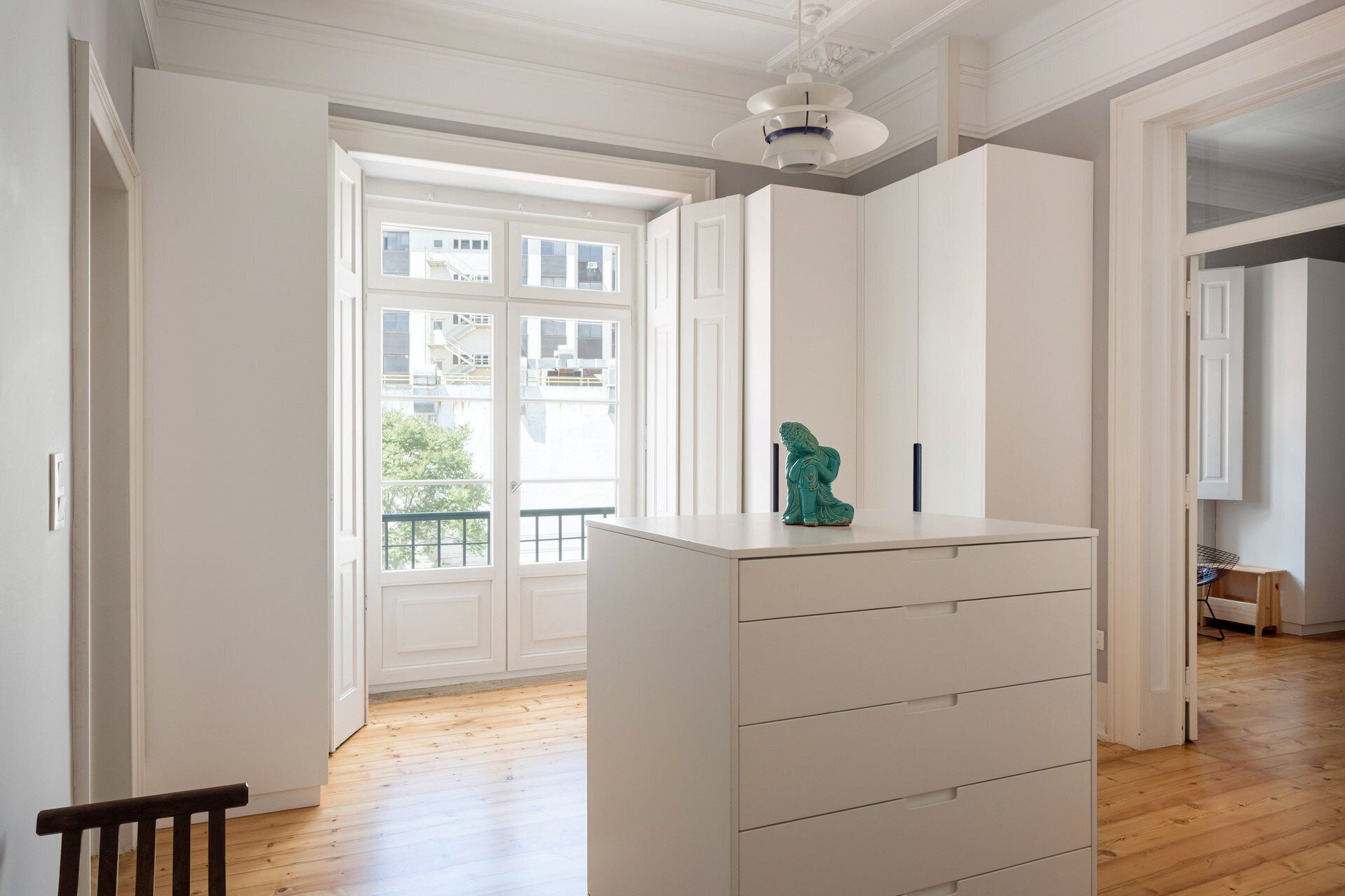 A room with a white dresser, a small statue, and a view through a large window.