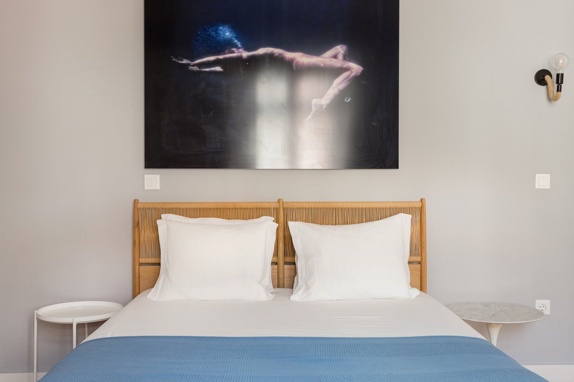 Ein Schlafzimmer mit einem Bett, zwei Kissen, einem Nachttisch, einer Wandleuchte und einem Bild.