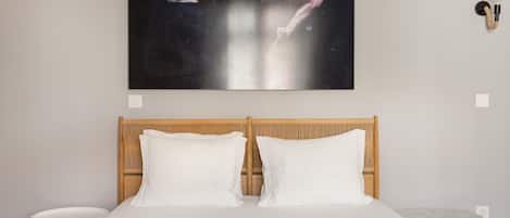 A bedroom with a bed, two pillows, a nightstand, a wall-mounted light, and a painting.