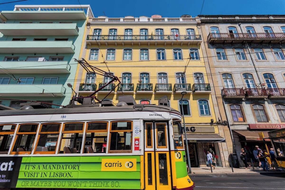 A tram with a 'carris' advertisement, passing by multi-story buildings with balconies.