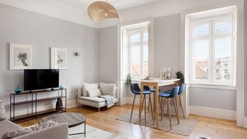 A living room with a sofa, TV, dining table with chairs, and artwork on the wall.