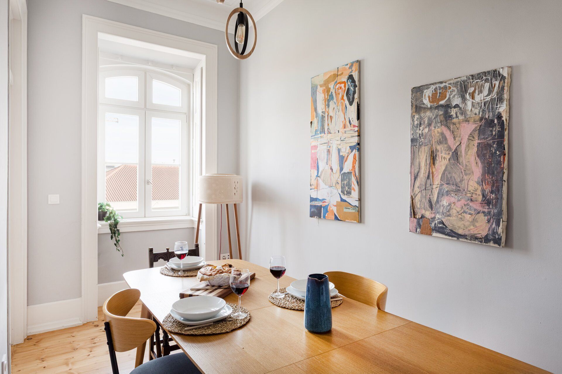 Un coin repas avec une table en bois, des chaises, un vase et des tableaux abstraits accrochés au mur.
