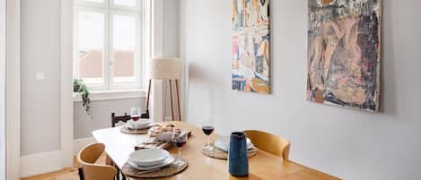 A dining area with a wooden table, chairs, a vase, and abstract paintings on the wall.