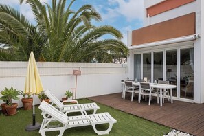 Eine Außenpatio mit weißen Liegestühlen, einem gelben Sonnenschirm und einem Tisch mit Stühlen.