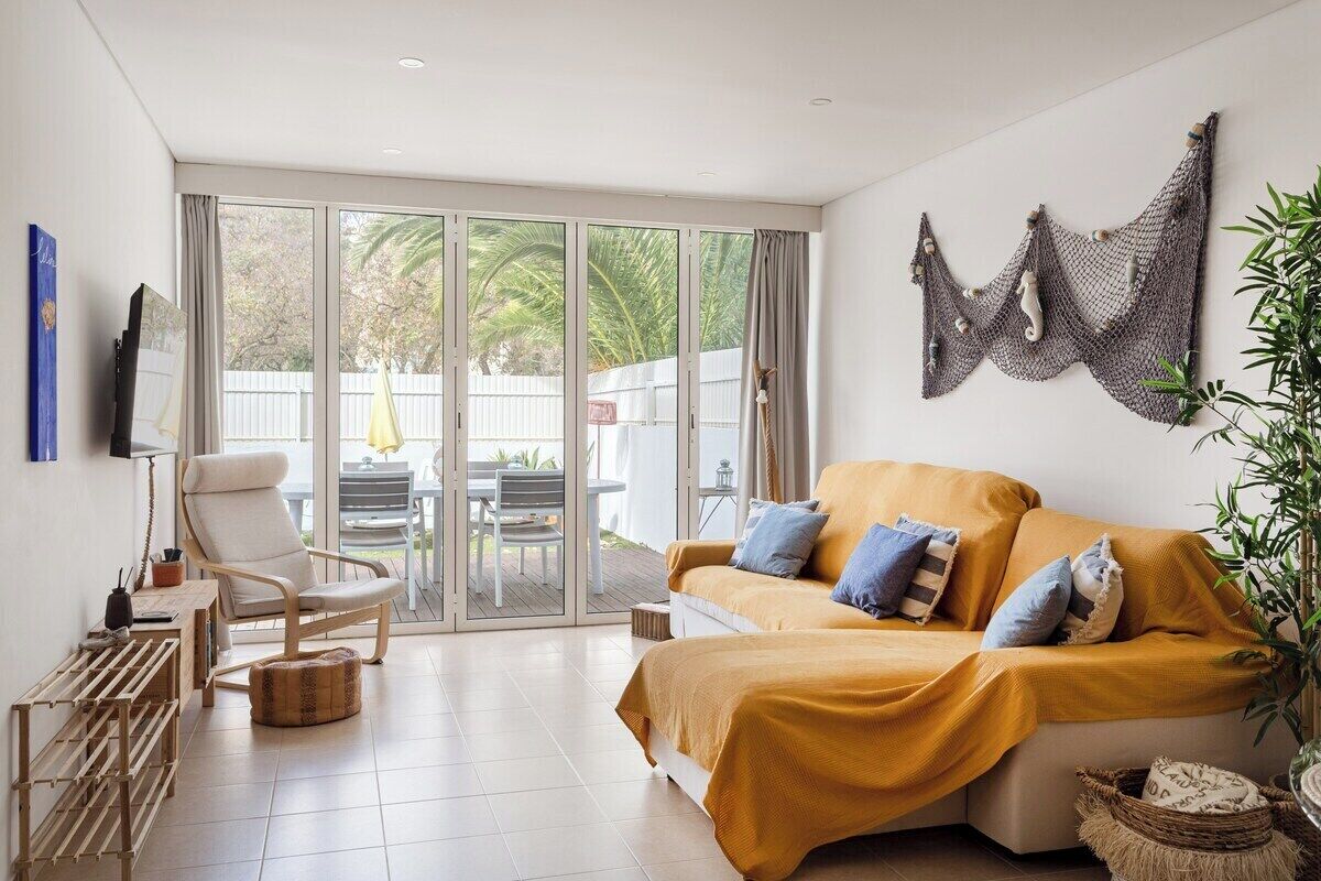 Una sala de estar moderna con un sofá, un sillón y un ventanal de vidrio que da a un espacio exterior.