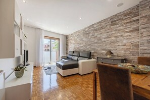 A modern living room with a sofa, a dining table, and a stone accent wall. - Casa Magó (Espinho)