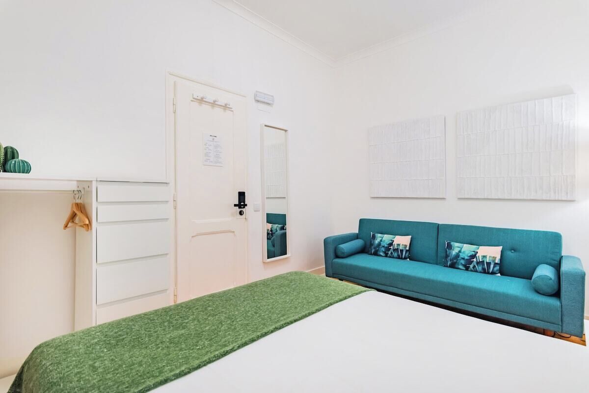 Una stanza con un letto, un divano blu, un armadio bianco e un tappeto verde.