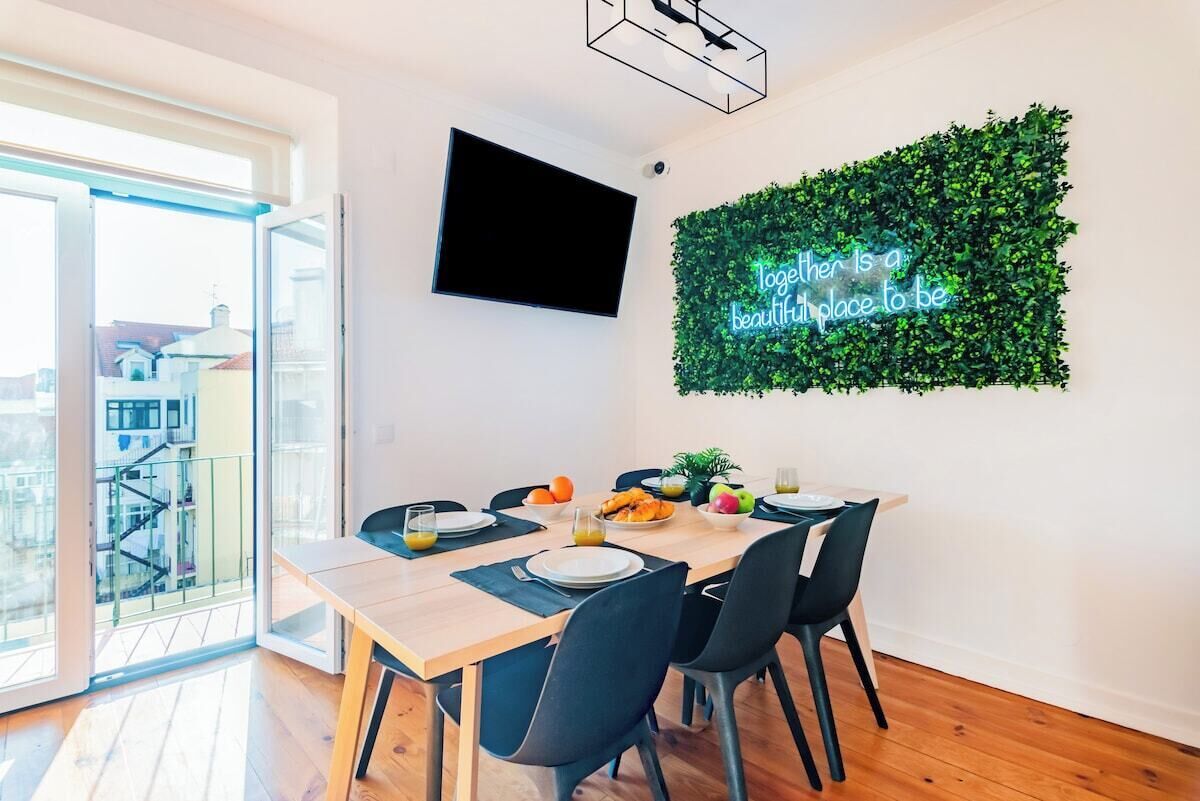 A dining area with a table set for four, a flat-screen TV mounted on the wall, and a neon sign.