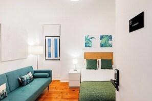 A room with a bed, a green sofa, a nightstand with a lamp, and a wall-mounted TV. - Double Room @ Guest Inn 2 Boutique House (campo pequeno)