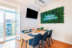 A dining area with a table set for four, a flat-screen TV mounted on the wall, and a neon sign above the table. - Double Room @ Guest Inn 2 Boutique House (campo pequeno)