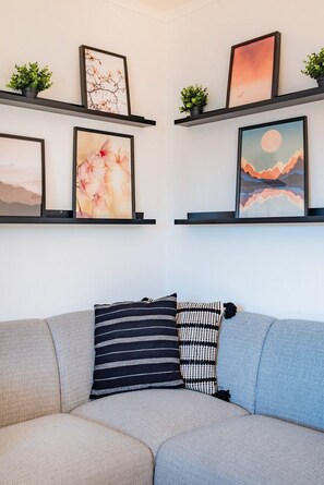 A living room with a sofa, two pillows, and framed artwork on shelves. - Double Room @ Guest Inn 2 Boutique House (campo pequeno)