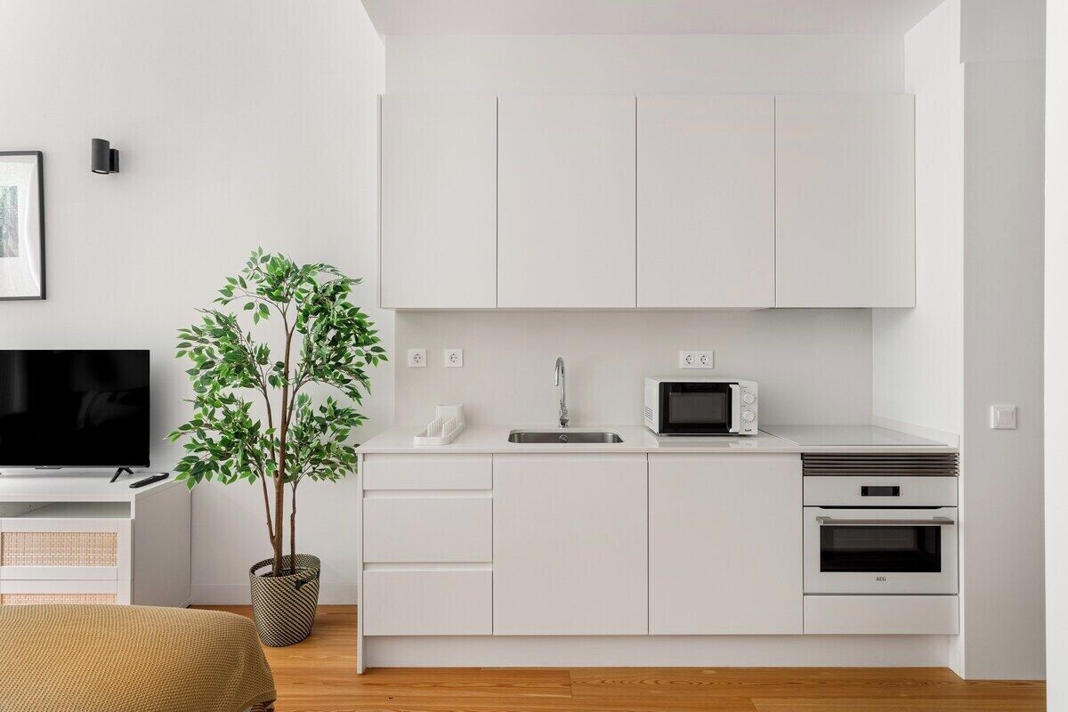 A modern kitchen with white cabinets, a microwave, an oven, and a sink.