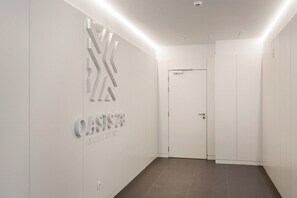 Ein Flur mit weißer Wand, einer Tür und einem Schild mit der Aufschrift 'OASIS 28 AV. CASAL FERRERO'.
