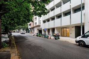 Ein mehrstöckiges Gebäude mit Parkplatz, einer von Bäumen gesäumten Straße und einem weißen Lieferwagen, der am Gehweg geparkt ist.