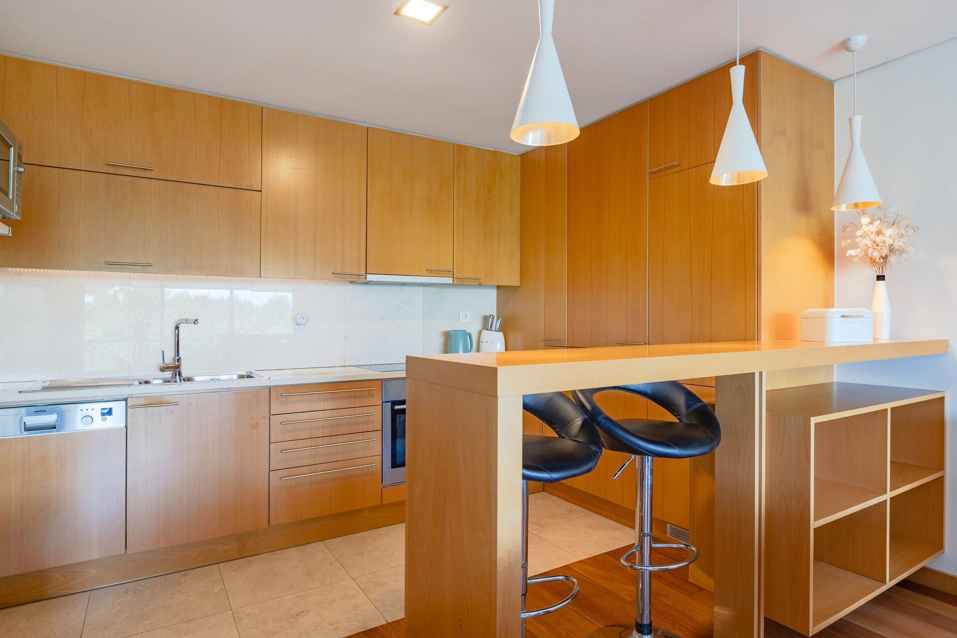 A modern kitchen with wooden cabinets, a built-in oven, a sink, and two bar stools.