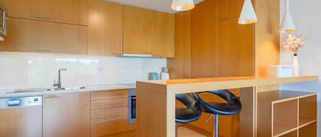 A modern kitchen with wooden cabinets, a built-in oven, a sink, and two bar stools.