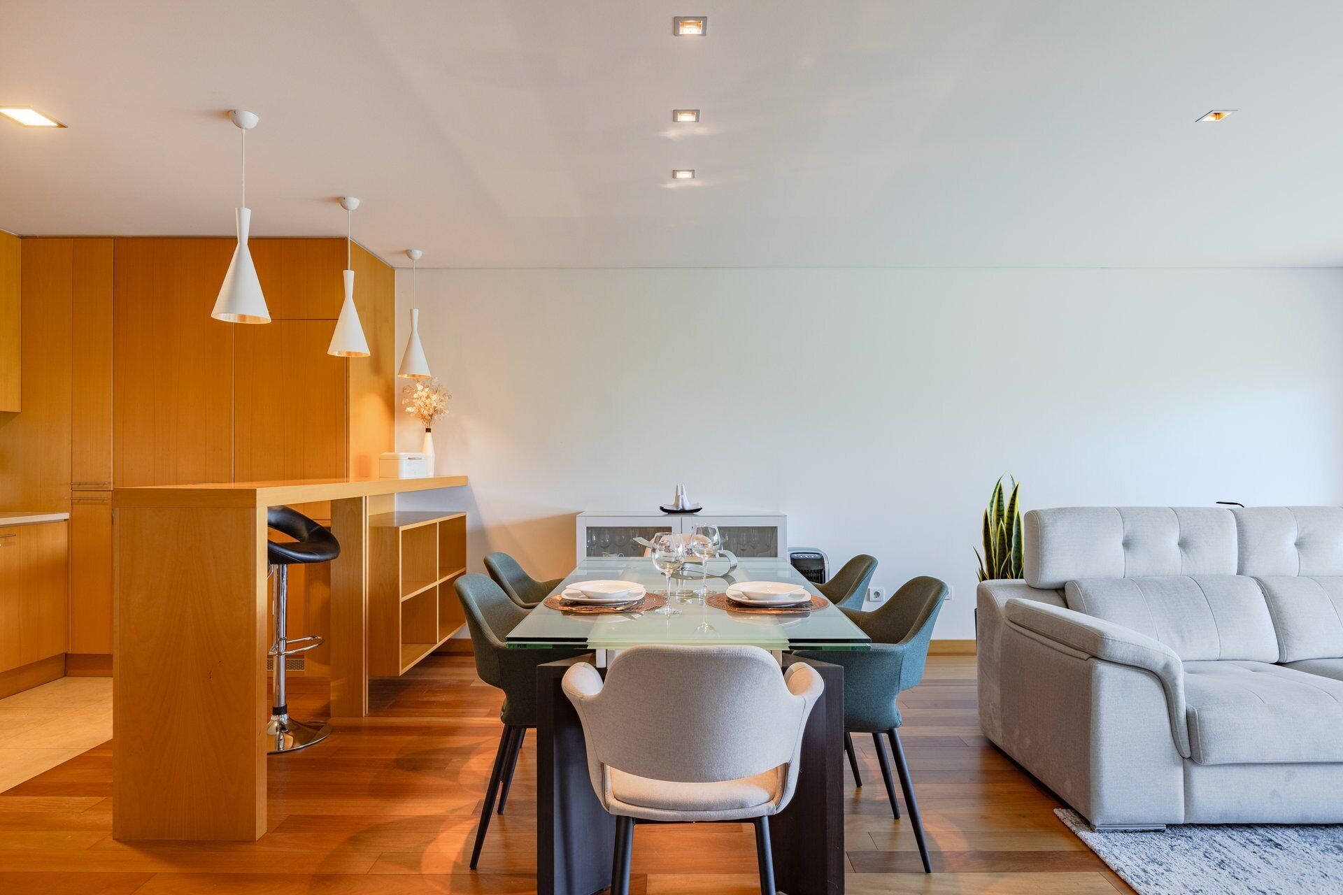 A modern dining area with a glass table, chairs, and pendant lighting.