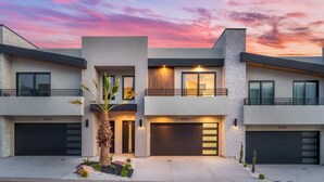 Een modern huis met twee verdiepingen, een garage, een balkon en een verzorgde voortuin.