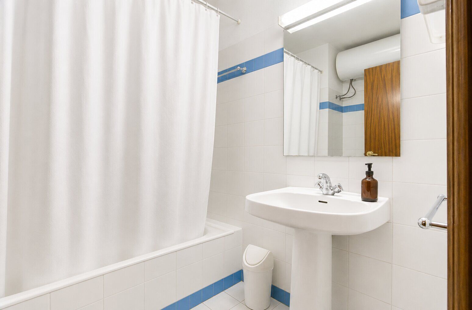 A bathroom with a white sink, a mirror, a shower curtain, and a trash bin.