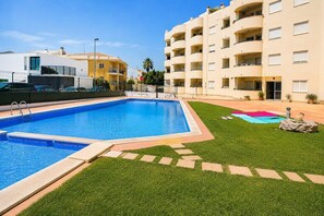 Ein Swimmingpool mit klarem, blauem Wasser, umgeben von einer gepflegten Rasenfläche und einigen Kübelpflanzen.
