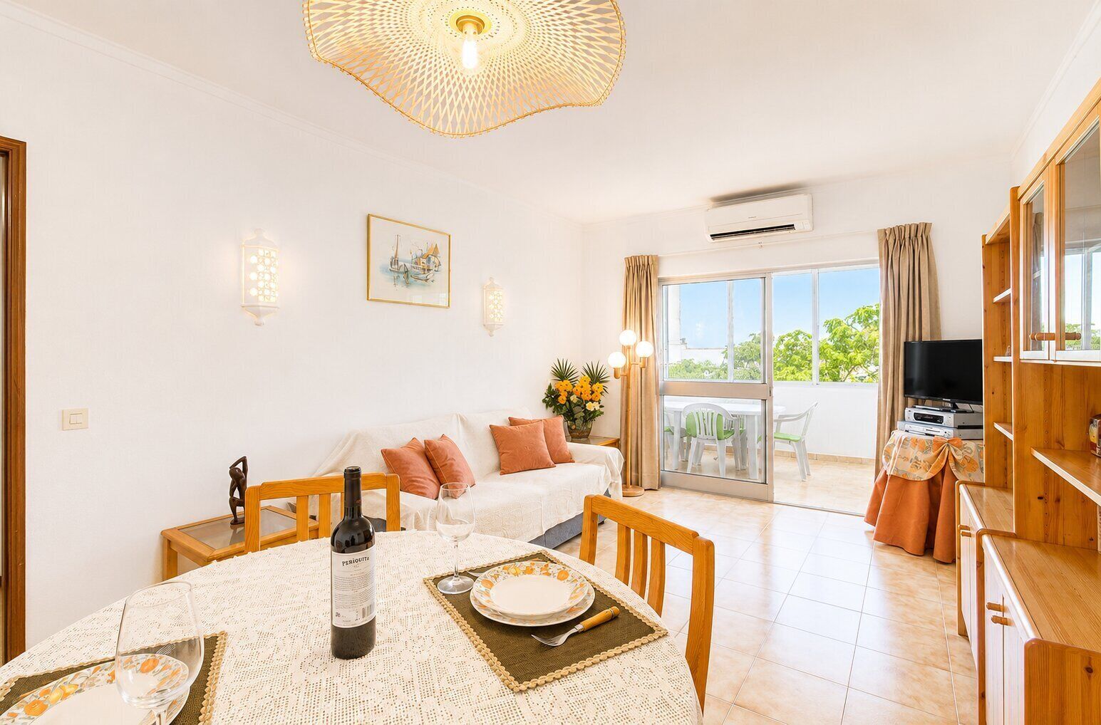 A dining area with a table set for two, a bottle of wine, and a painting on the wall.