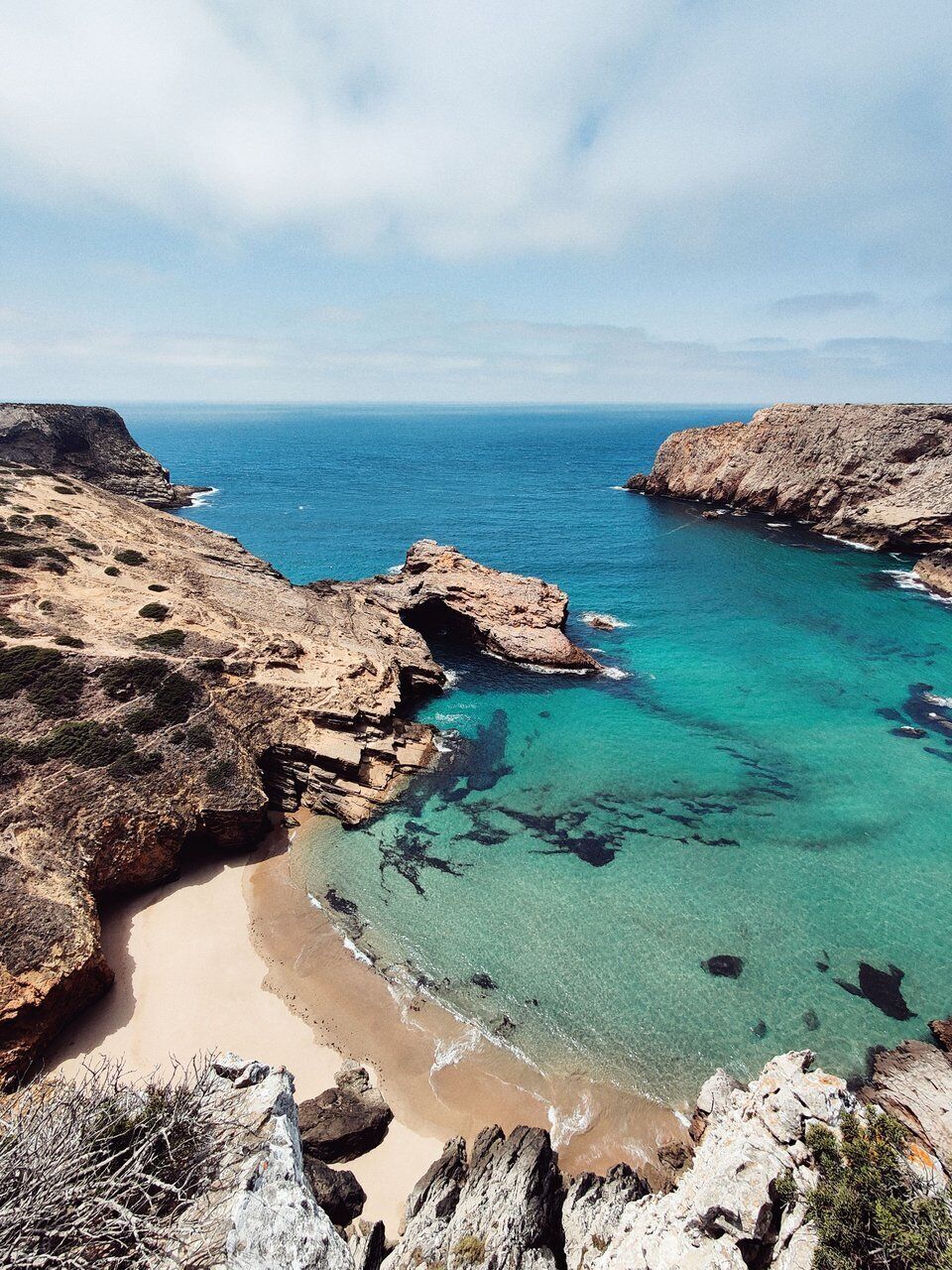 A coastal landscape with rocky cliffs, clear turquoise waters, and a sandy beach.