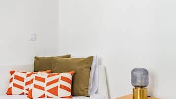 Ein Bett mit weißer Bettwäsche und orangefarbenen und braunen Kissen, ein Nachttisch mit Lampe und ein grüner Teppich.