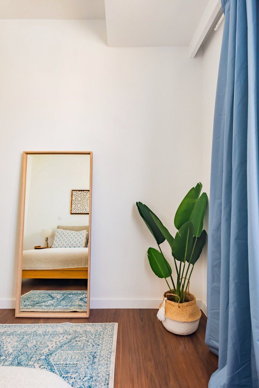 Una stanza con un letto, uno specchio, una pianta in vaso, una tenda blu e un tappeto decorato.