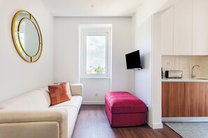 Een modern appartement met een bank, een rode poef, een televisie en een keukenhoek.