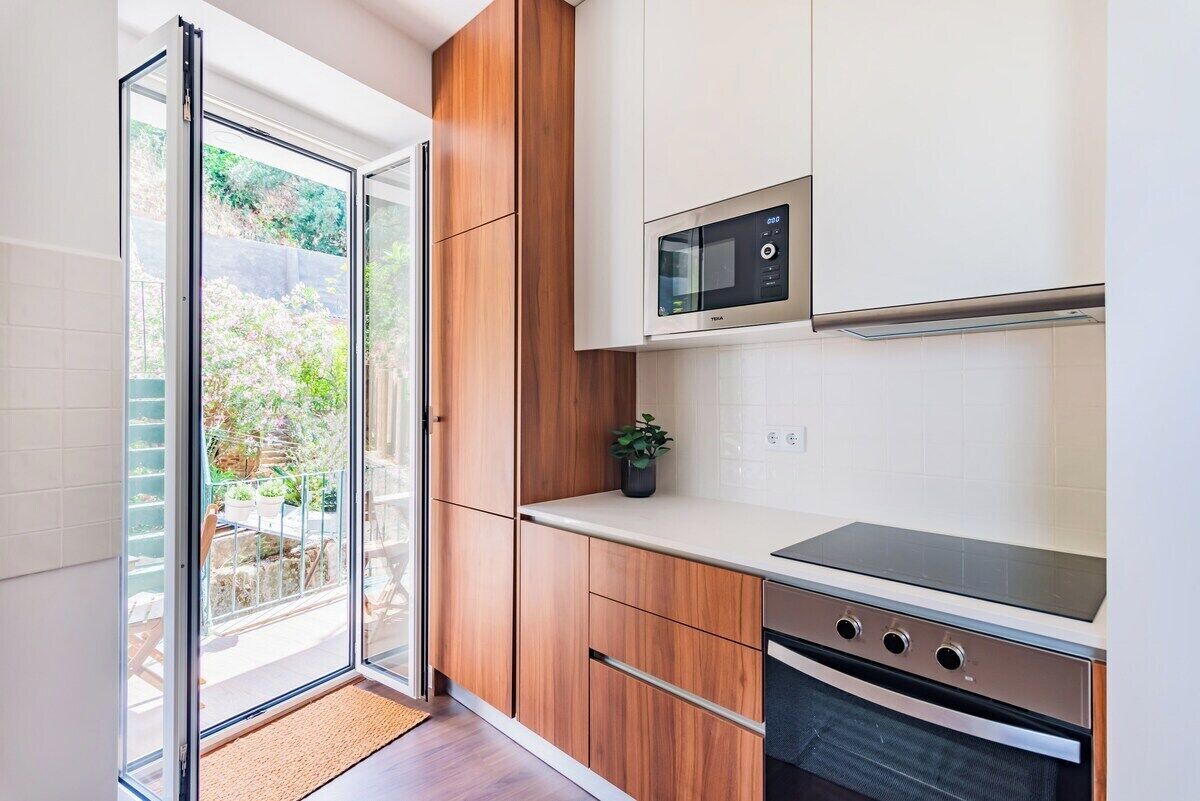 A modern kitchen with a sliding glass door leading to a balcony, a built-in microwave, and a stainless steel oven.