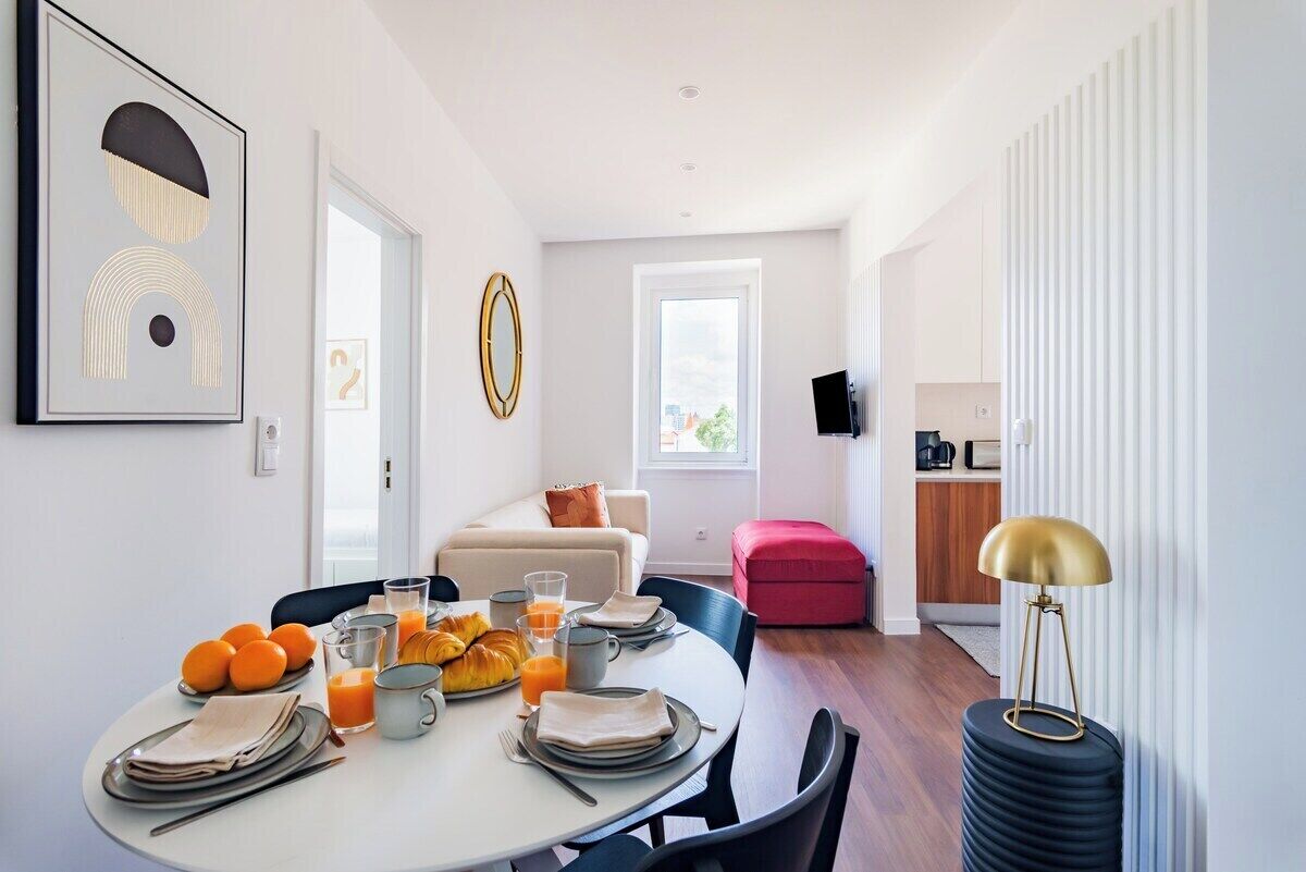 Ein moderner Essbereich mit einem runden Tisch, gedeckt für das Frühstück, einer Couch und einer Küche im Hintergrund.