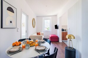 Et moderne spiseområde med et rundt bord dækket til morgenmad, en sofa og et køkken i baggrunden.