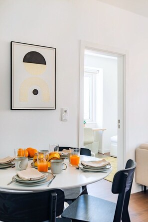 Een eetgedeelte met een ronde tafel gedekt voor het ontbijt, een kunstwerk in een lijst aan de muur, en een deur die naar een andere kamer leidt.