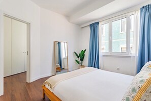 Et soveværelse med seng, et spejl, et vindue med gardiner og en dør.
