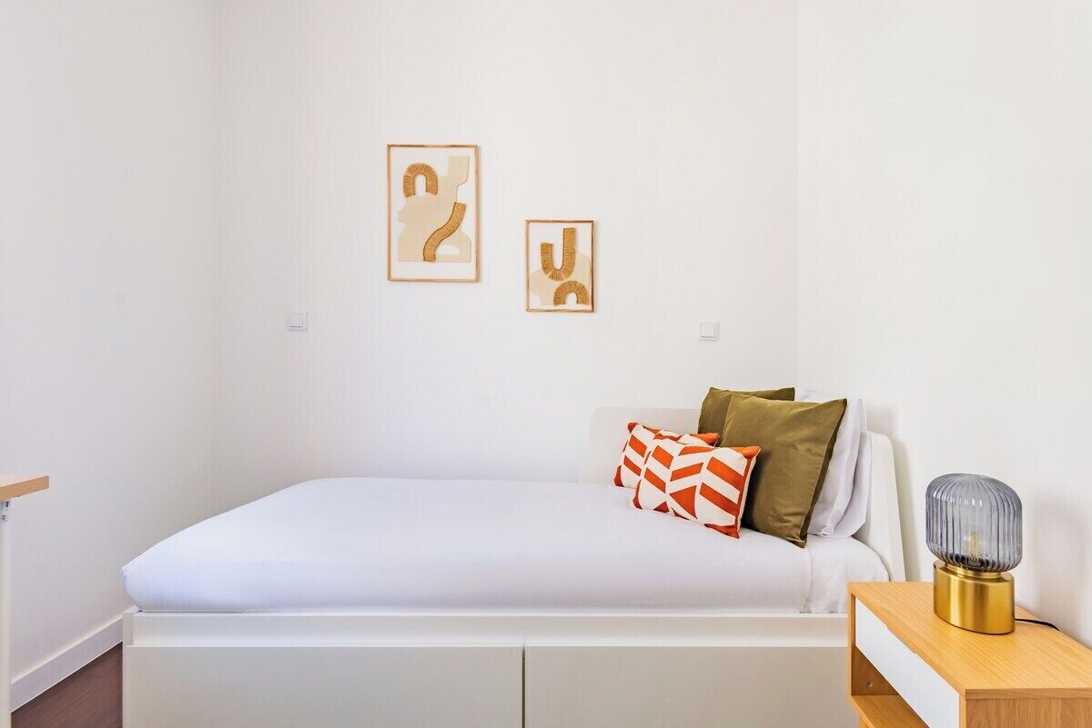 Una camera da letto ordinata con un letto, cuscini, un comodino e decorazioni a parete.