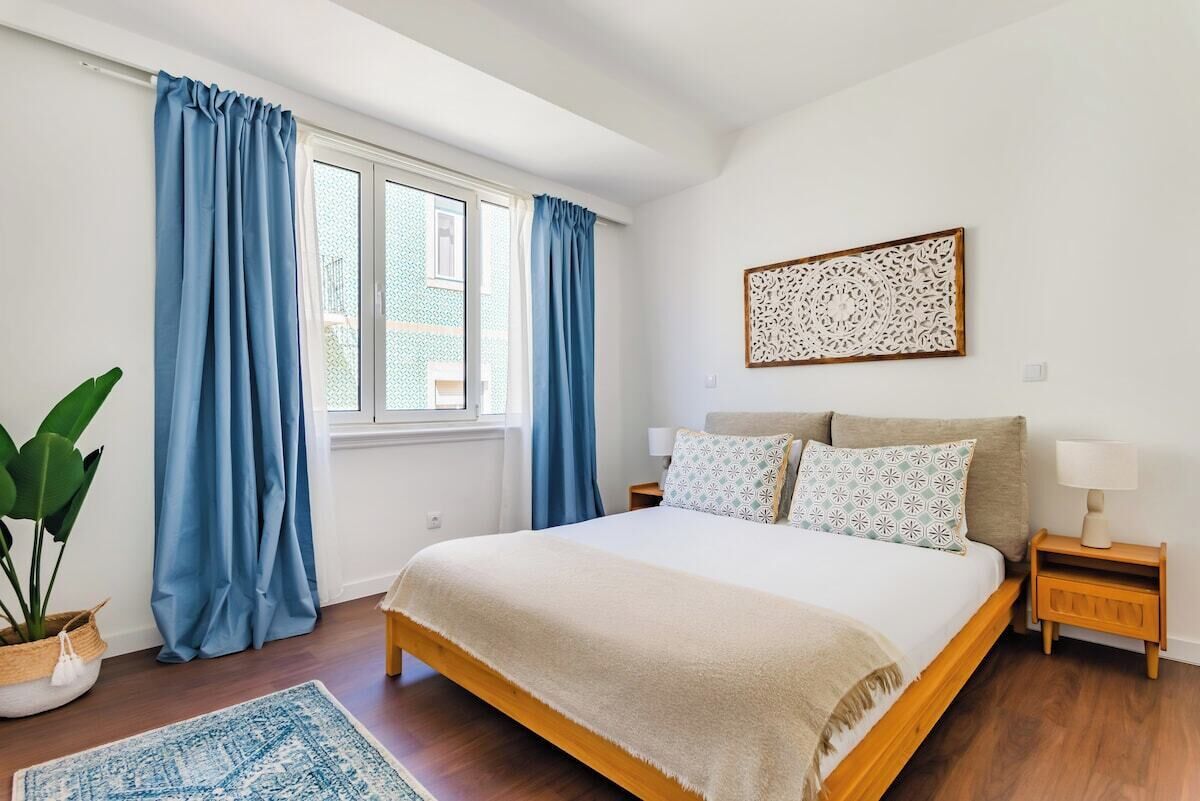 Une chambre à coucher comprenant un lit, une table de chevet, une lampe, une fenêtre avec des rideaux et un élément décoratif fixé au mur.