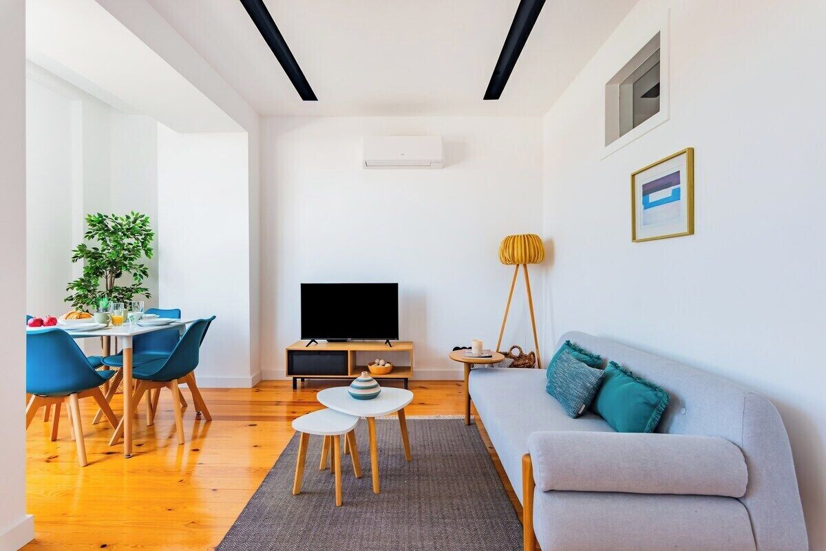 Ein modernes Wohnzimmer mit einer Couch, einem Fernseher, einem Esstisch, Stühlen und einer Pflanze.