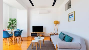 Ein modernes Wohnzimmer mit einer Couch, einem Fernseher, einem Esstisch, Stühlen und einer Pflanze.