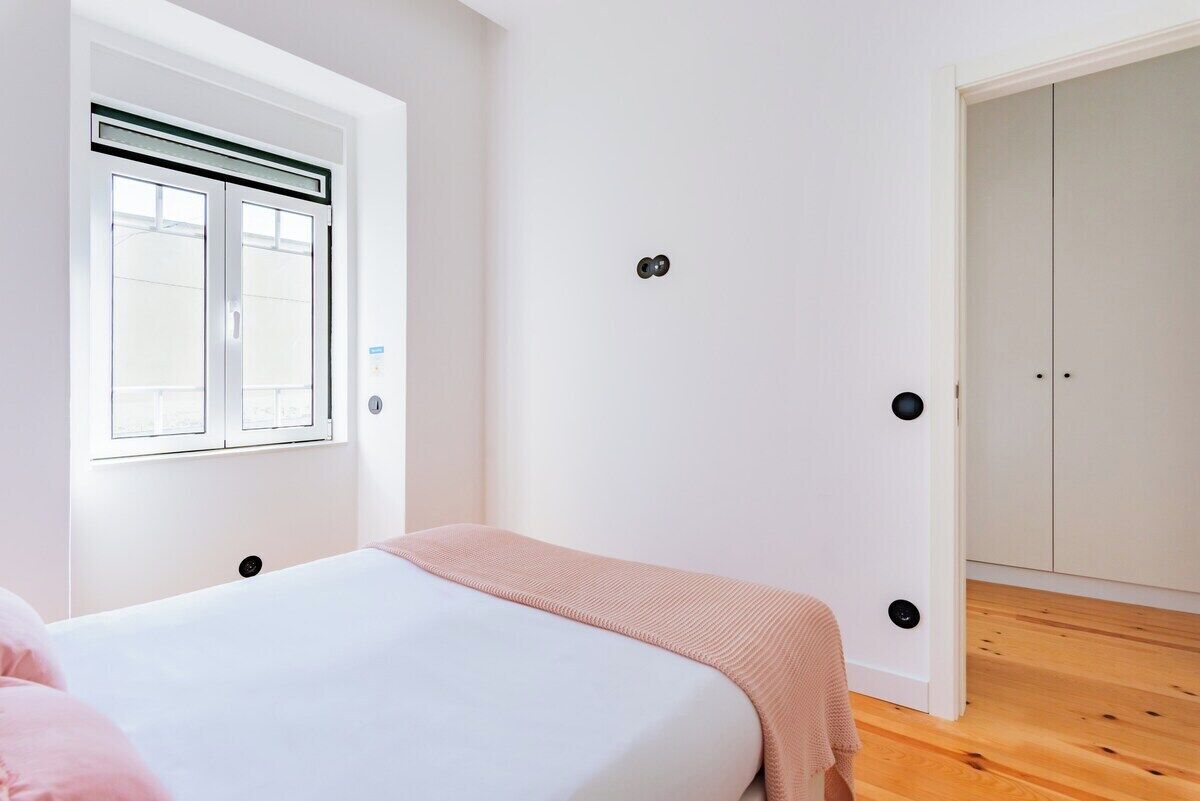 Um quarto com cama, janela, porta e guarda-roupa.